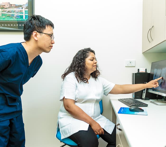 A dentist discussing a dental model with a person in a treatment room.