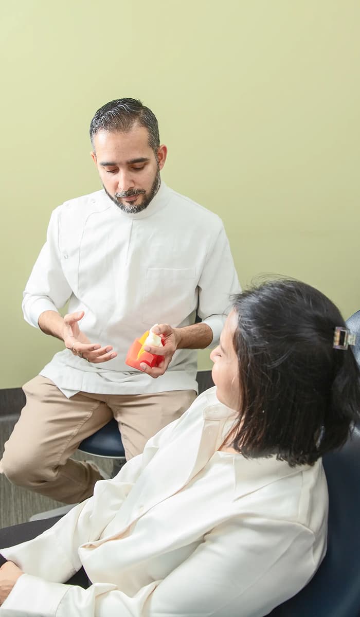 A clinician holding a dental model while speaking with a seated person.