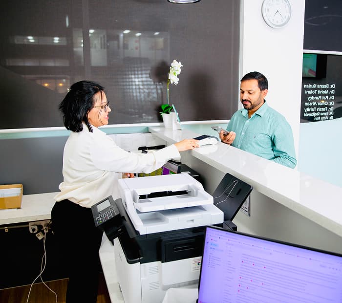 A dentist showing a dental model to a seated person in a treatment room.