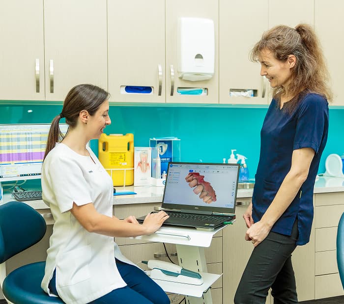 A dental professional discussing information on a laptop with a patient in a dental room