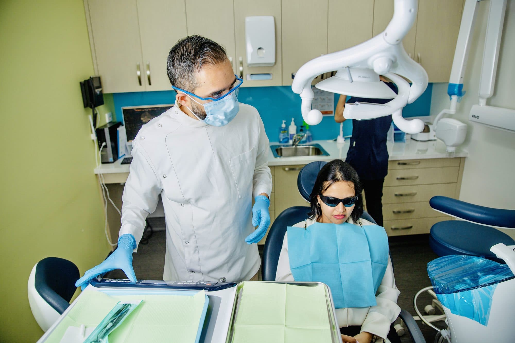 A dentist speaking with a patient in a treatment room.