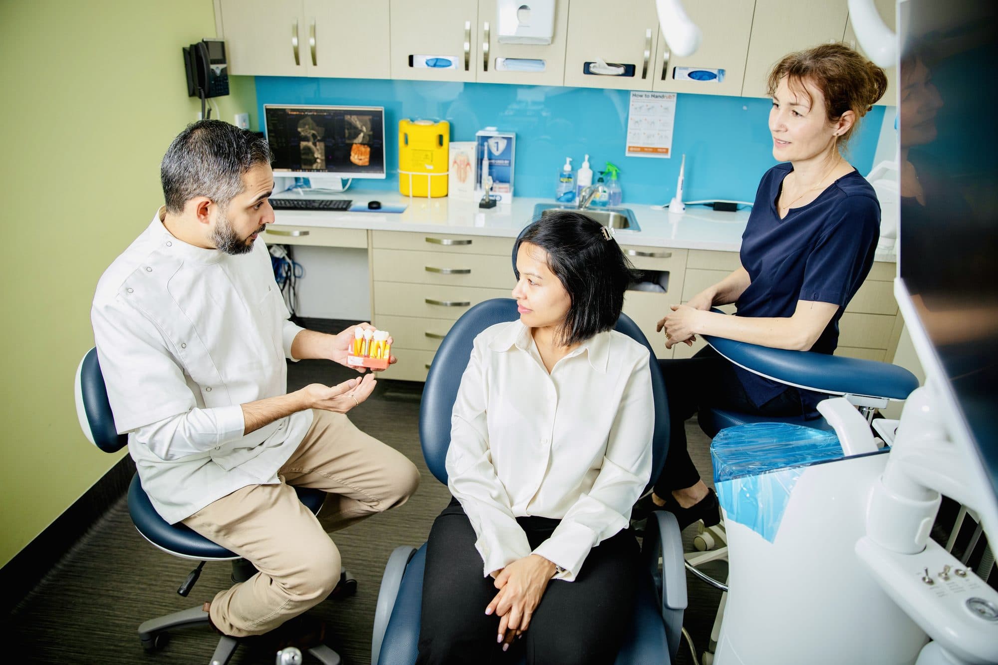 A dentist holding a dental model while speaking with a seated person.
