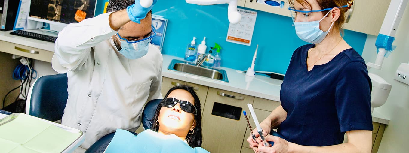 A dentist and dental assistant providing care to a patient in a treatment room.
