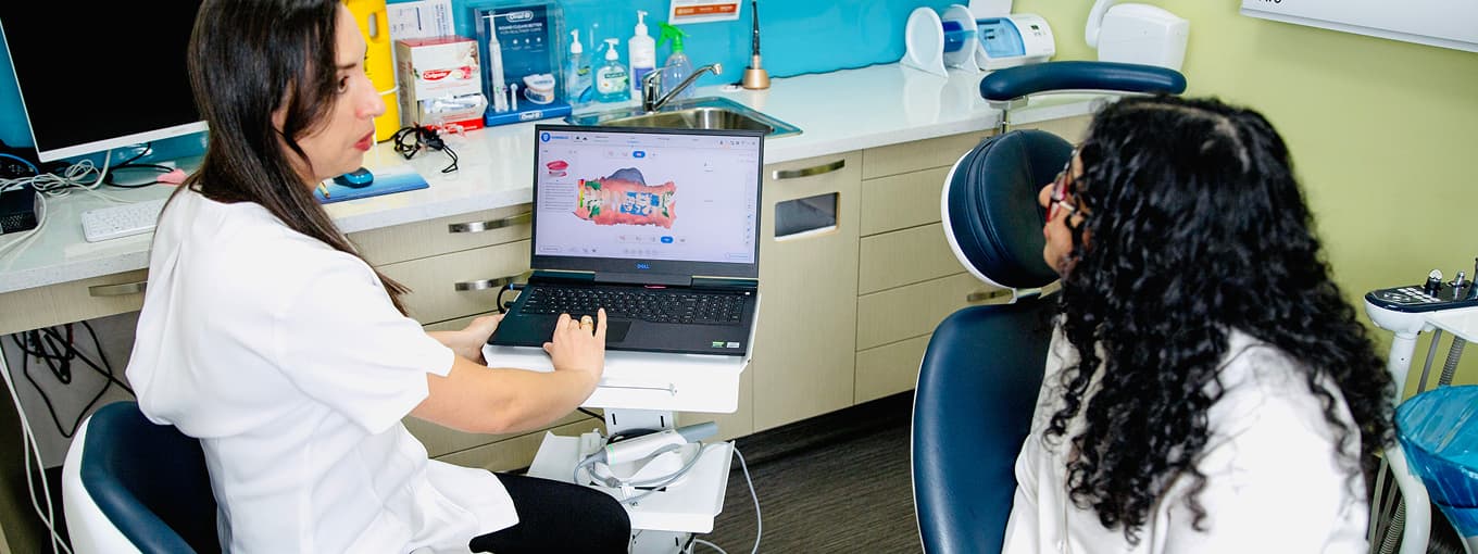 A clinician discussing a dental scan with a seated person in a treatment room.