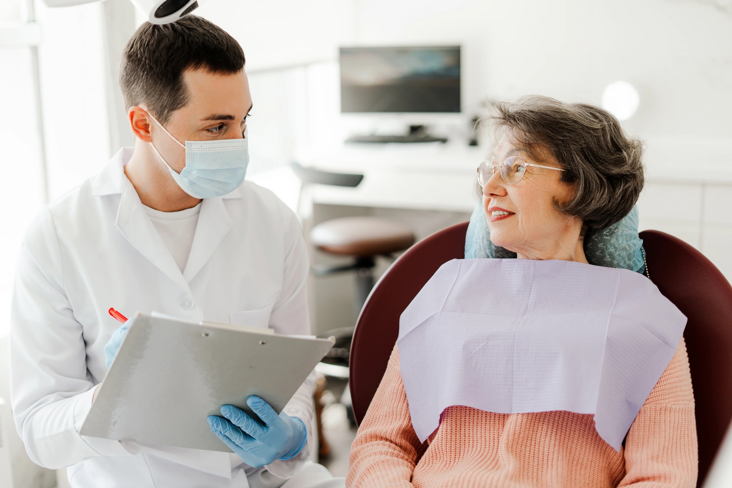 A dentist discussing care with an older patient in a treatment room.